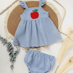 A baby girl's blue and white striped summer outfit featuring a red apple applique on the chest and ruffle sleeve top, paired with matching shorts, laid flat on a woven mat.