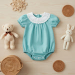 Green baby girl bunny romper set with bubble sleeves, white embroidered collar, teddy bear, and plush rabbit toy on a wooden background.