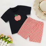 Flat lay of toddler baby boy back to school outfit featuring a black short sleeve t-shirt with a red apple applique design and matching red gingham shorts
